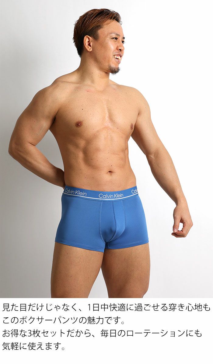 男性モデルがCalvin Kleinのブルーのローライズボクサーパンツを着用。 通気性に優れたマイクロファイバー素材で、1日中快適な着心地の3枚セット。 商品名：カルバンクライン CK Microfiber Plus メンズ下着。